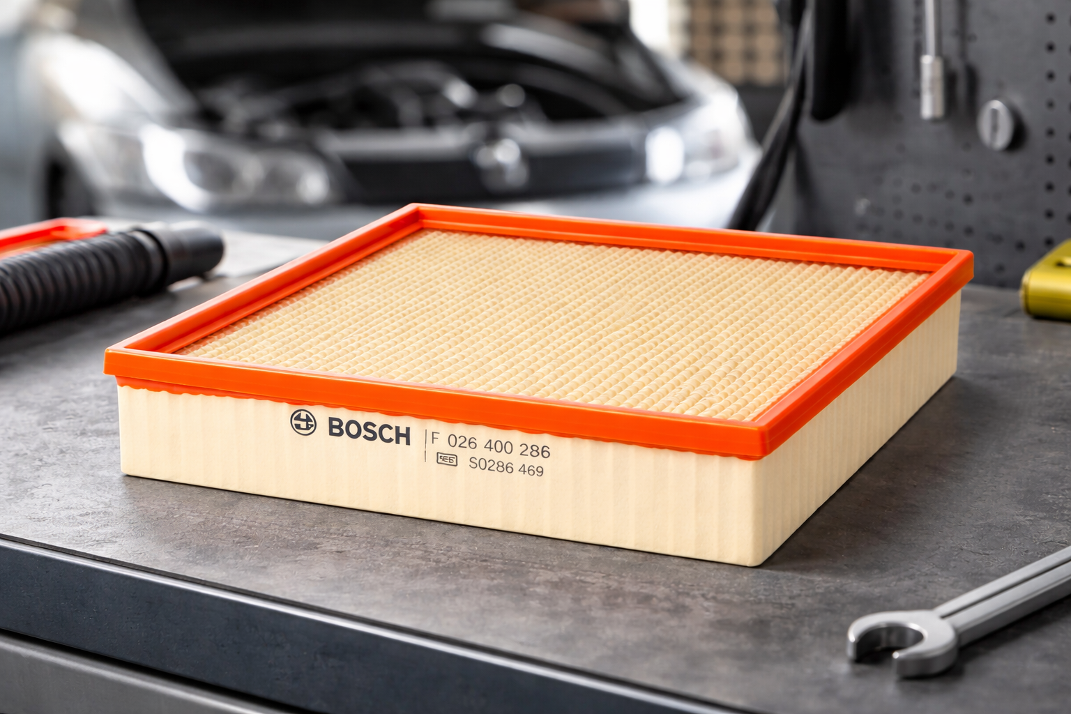 The Bosch air filter placed on a dark surface in front of an open car engine bay, illustrating its real-world application.